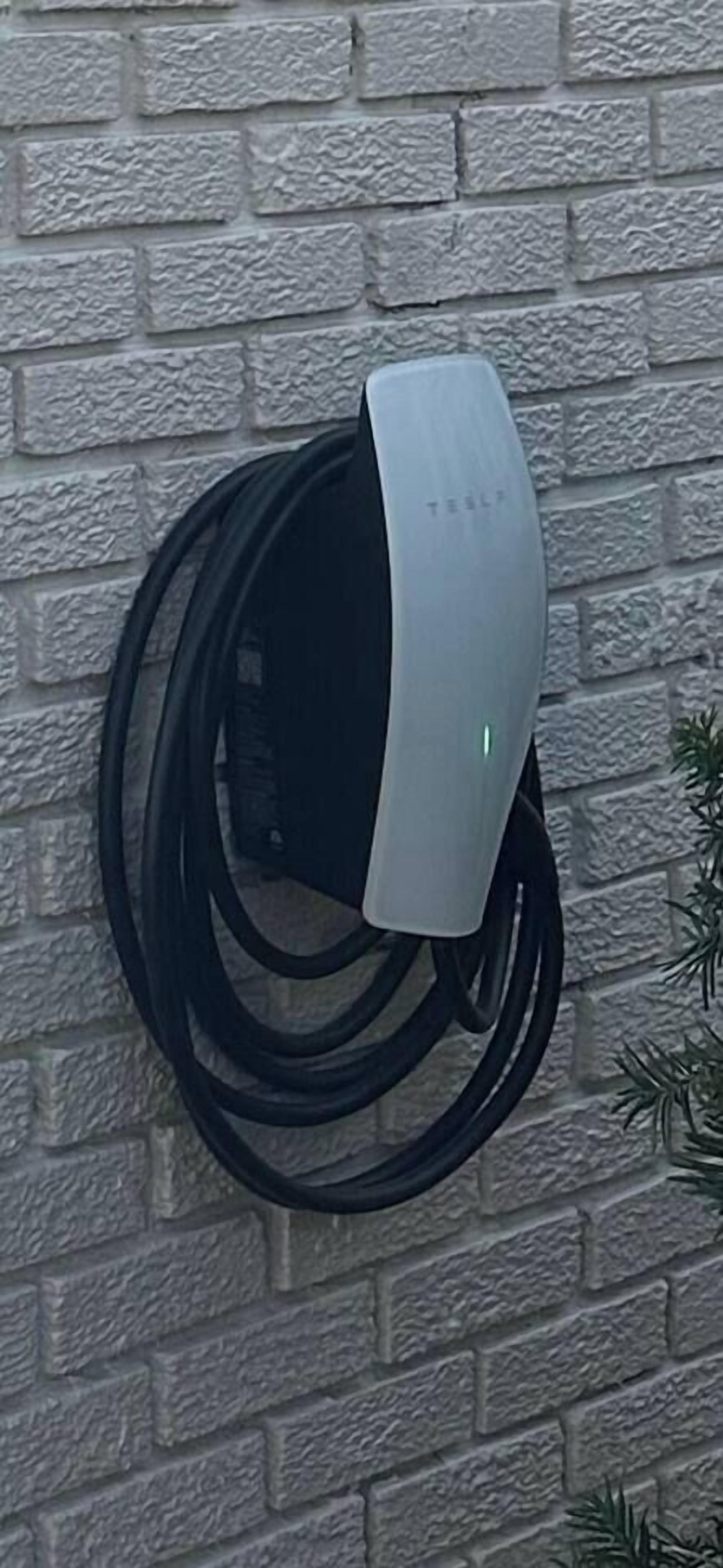 En vægmonteret Tesla-ladestation med et kabel viklet omkring sig.