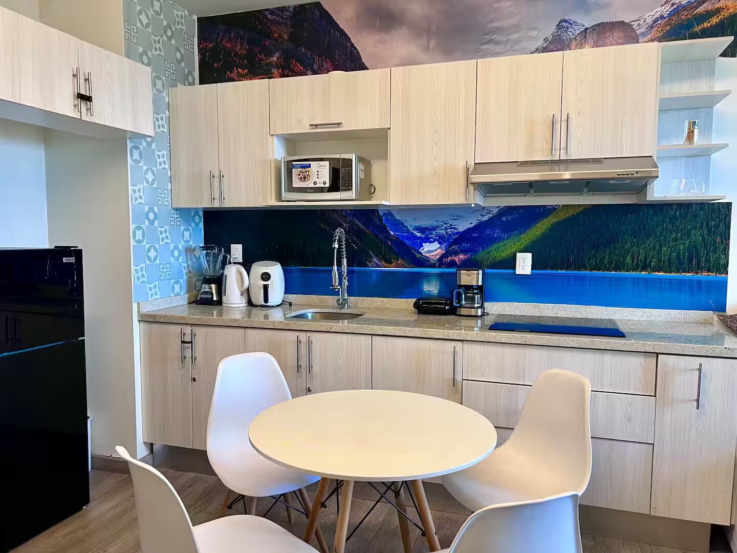 A modern kitchen with a microwave, coffee maker, and a scenic mural on the wall.