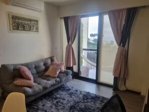 Een woonkamer met een grijze bank, een kamerbreed vloerkleed en een balkon met gordijnen.
