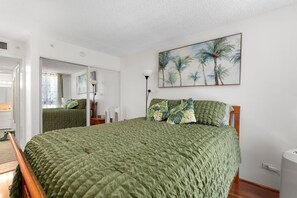 Ein Schlafzimmer mit einem großen Bett, einem Spiegel, einem Palmen-Gemälde und einer Nachttischlampe.