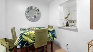 A dining area with a round table, chairs, a clock, and a window with a plant. - Waikiki Beach Airbnb | Pool, Parking,Walk to Beach (Honolulu)