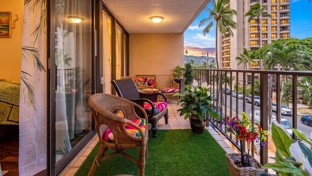 A balcony with wicker chairs, a small table, and potted plants. - Waikiki Beach Airbnb | Pool, Parking,Walk to Beach (Honolulu)