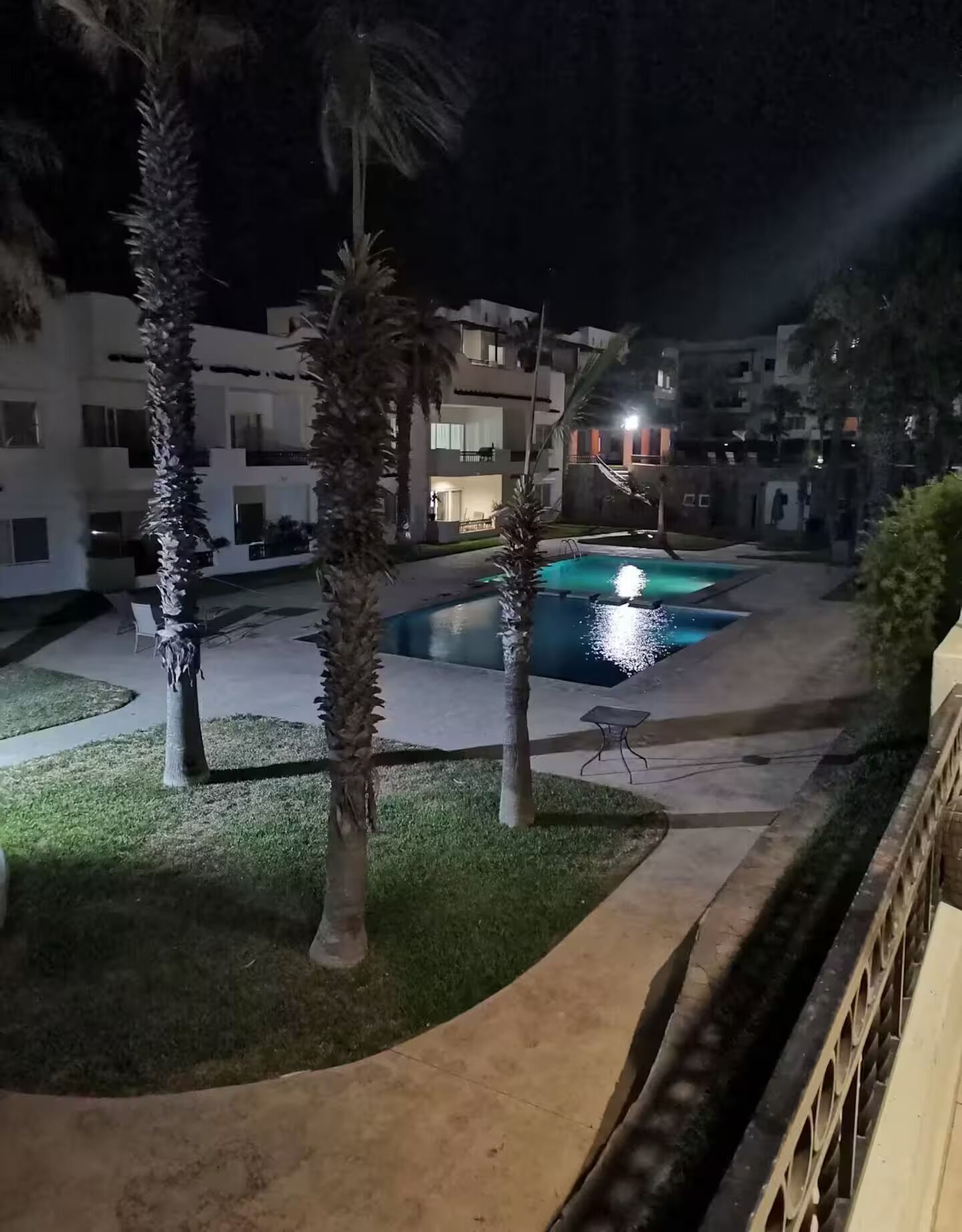Ein Nachtbild von einem Poolbereich mit Palmen und einem Gebäude im Hintergrund.