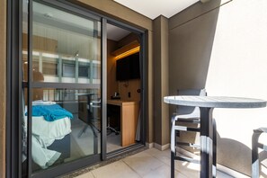 A hotel room with a sliding glass door leading to a balcony, a small table, and a chair. - Studio com Varanda a 200m da Paulista e do Masp (São Paulo)
