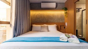 A hotel room with a bed, a window with curtains, an air conditioning unit, and a small plant. - Studio com Varanda a 200m da Paulista e do Masp (São Paulo)