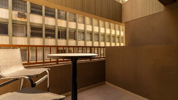 A balcony with a table and two chairs, overlooking a building with multiple windows. - Studio Perto da Av Paulista e Masp Jardim Paulista (São Paulo)