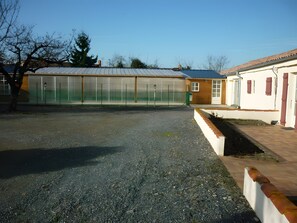 A building with a fenced sports court, a gravel driveway, and a small garden area. - Le Paradis - Guest Room C (Chaillé-les-Marais)