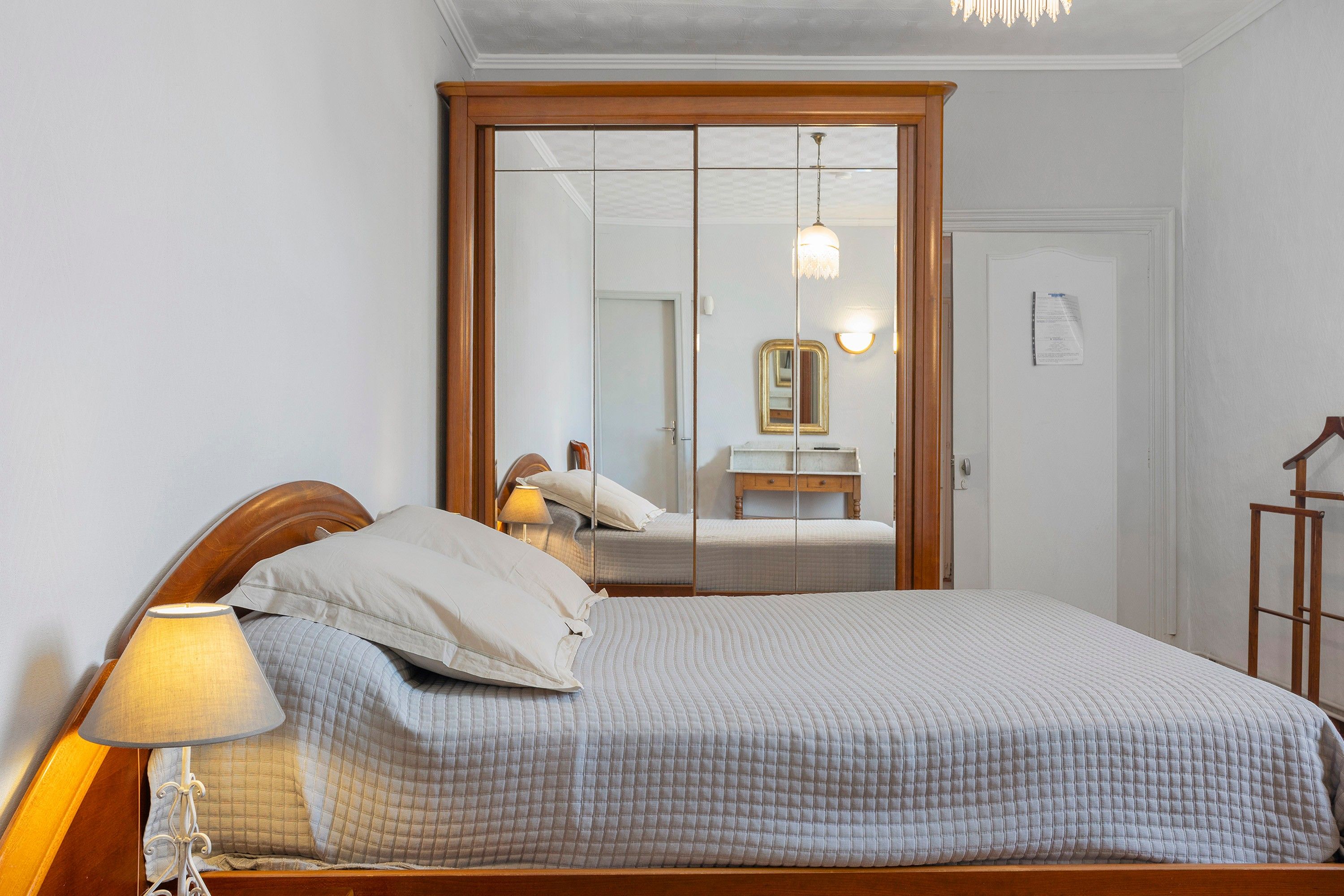 A bedroom with a bed, a nightstand, a lamp, a mirror, and a wardrobe.