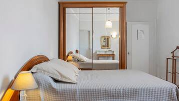 A bedroom with a bed, a nightstand, a lamp, a mirror, and a wardrobe.