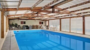 Une piscine dotée d’un plafond et de murs en bois, entourée de chaises longues et d’une table.