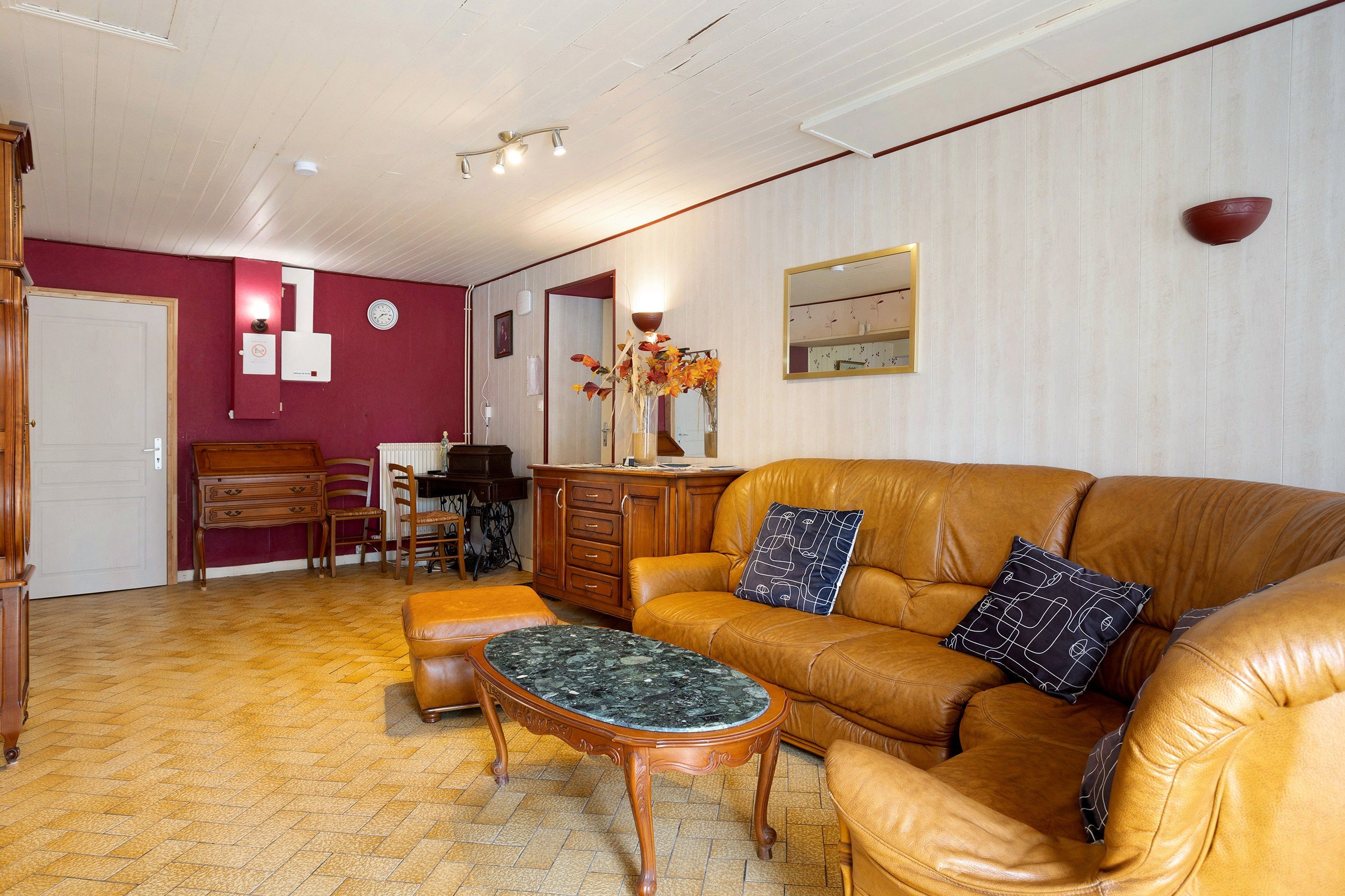 A living room with a brown leather sofa, a wooden coffee table, and a dining area with a wooden table and chairs.