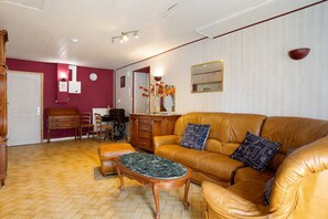Una sala de estar con un sofá de cuero marrón, una mesa de centro de madera y una zona de comedor con una mesa y sillas de madera.