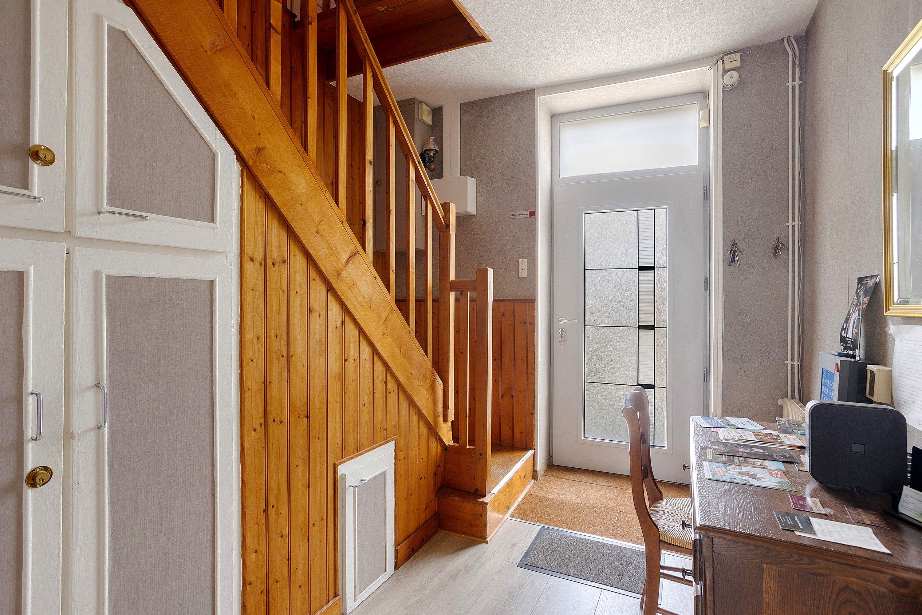 Uma escada de madeira leva a um quarto com uma porta, uma escrivaninha com papéis e uma cadeira.