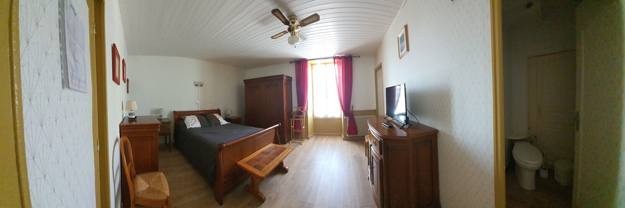 A room with a bed, a desk, a chair, a television, and a window with curtains.