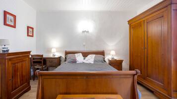 A bedroom with a wooden bed, bedside lamps, a nightstand, a wardrobe, and a desk with a chair.