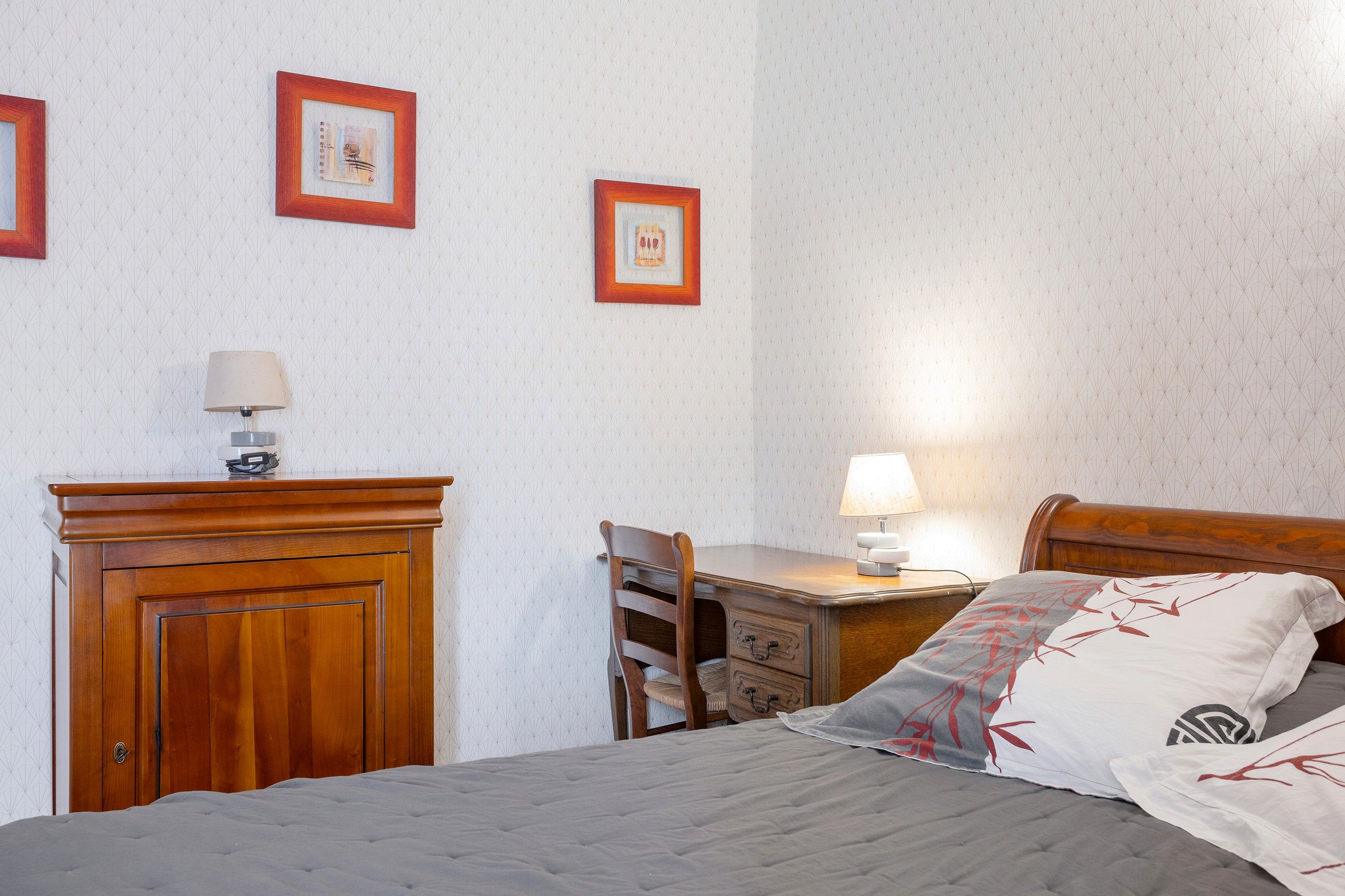 Une chambre à coucher avec un lit, un bureau et deux chaises. Deux tableaux encadrés sont accrochés au mur.