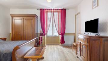 Une chambre à coucher avec un lit, une commode en bois, un téléviseur et une fenêtre avec des rideaux.