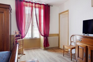 Une pièce avec une armoire en bois, un téléviseur posé sur un meuble en bois, un radiateur et une fenêtre avec des rideaux rouges.