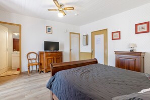 Un dormitorio con una cama, un televisor sobre un aparador de madera, una silla y un ventilador de techo.