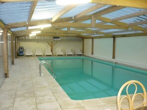 An indoor swimming pool with clear water, surrounded by white lounge chairs, and a tiled floor.