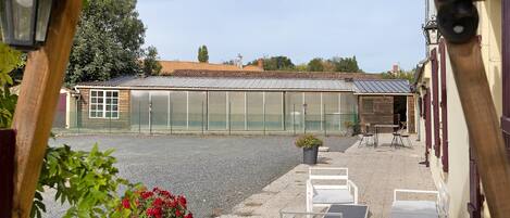 A greenhouse with a metal roof, a gravel ground, and a row of white chairs and tables.