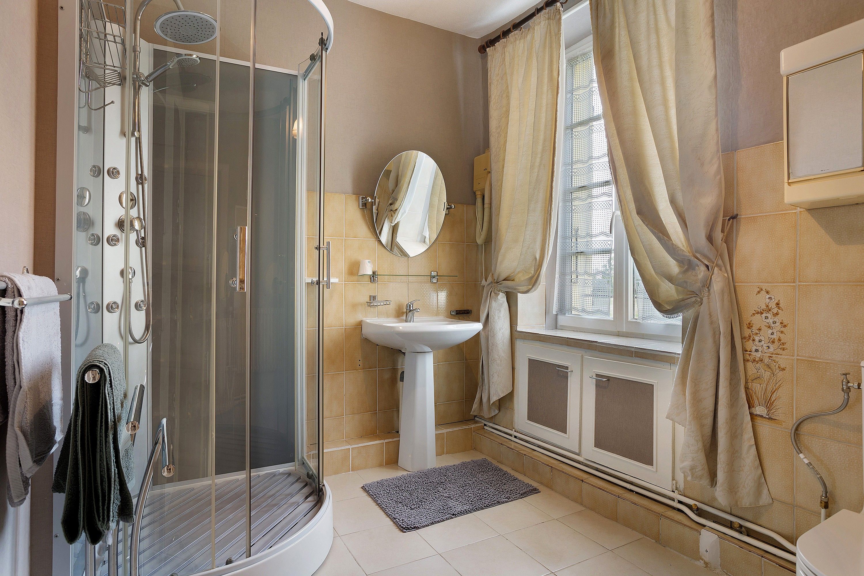 Une salle de bain avec une douche à parois de verre, un lavabo, un miroir et une fenêtre avec des rideaux.