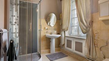 Une salle de bain avec une douche à parois de verre, un lavabo, un miroir et une fenêtre avec des rideaux.