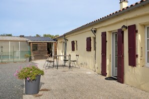 A building with a gravel driveway, a wooden door, and a window with shutters.
