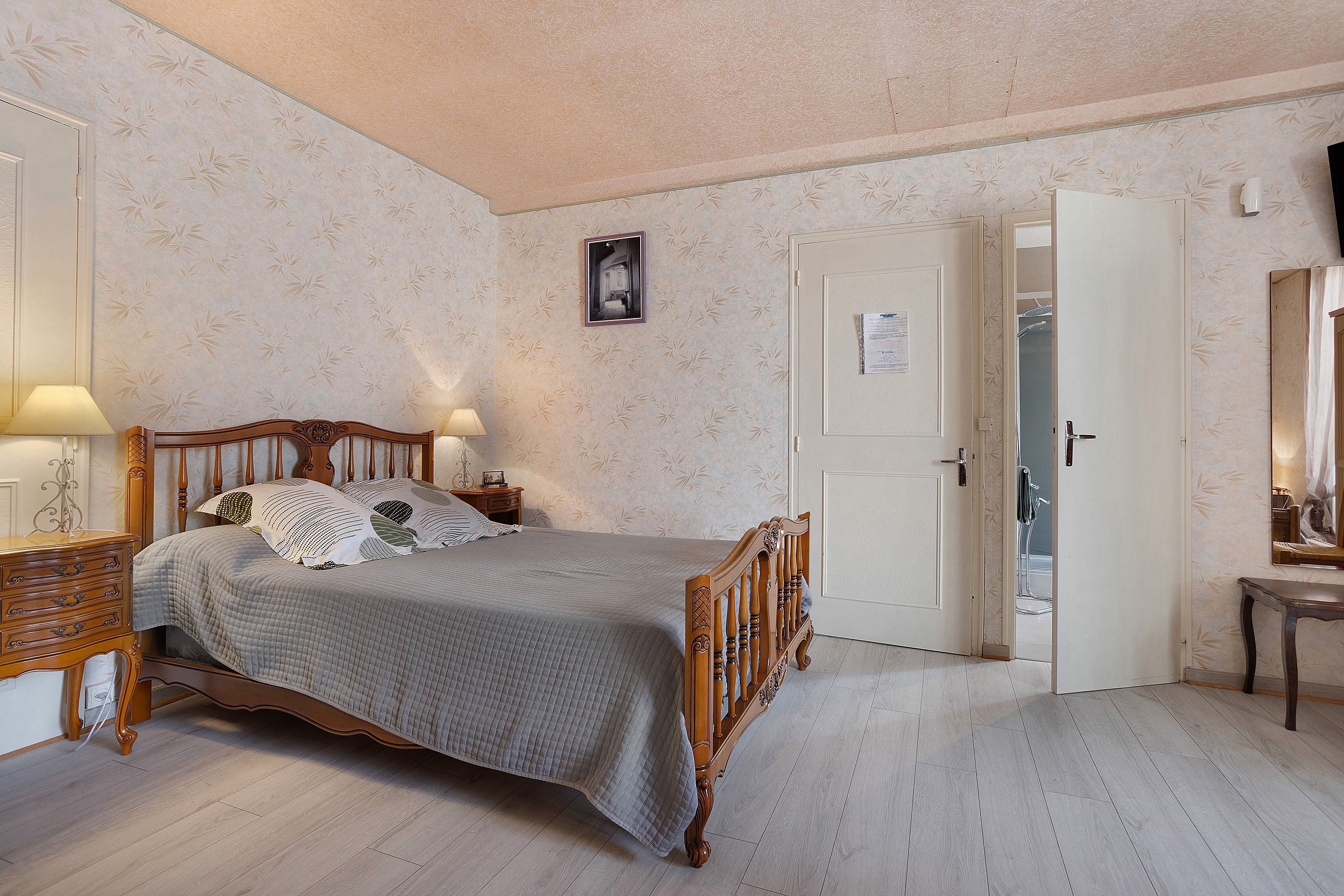 Een slaapkamer met een houten bed, een nachtkastje, een lamp en een deur naar een badkamer.