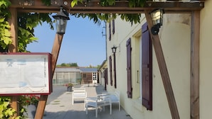 A courtyard with a wooden pergola, white chairs, and a signboard.