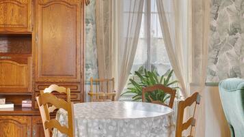 Uma sala de jantar com mesa redonda, cadeiras de madeira, um armário e janela com cortinas.