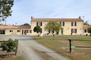 A two-story building with a tiled roof, a gravel driveway, and a sign indicating 'CHAMBRES D'HOTES' (rooms for rent).