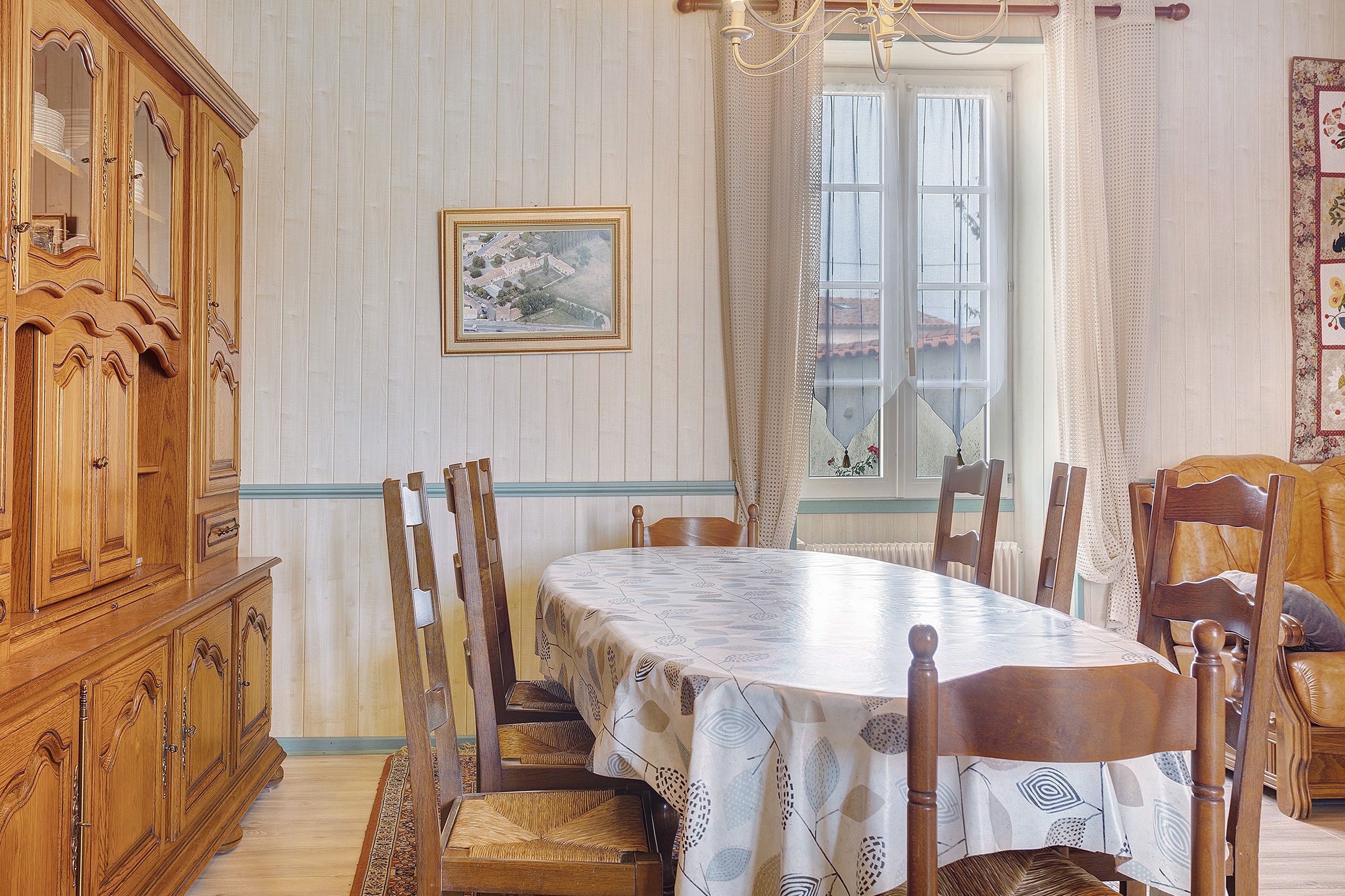 Uma sala de jantar com uma grande mesa de madeira, cadeiras, um armário e uma janela com cortinas.