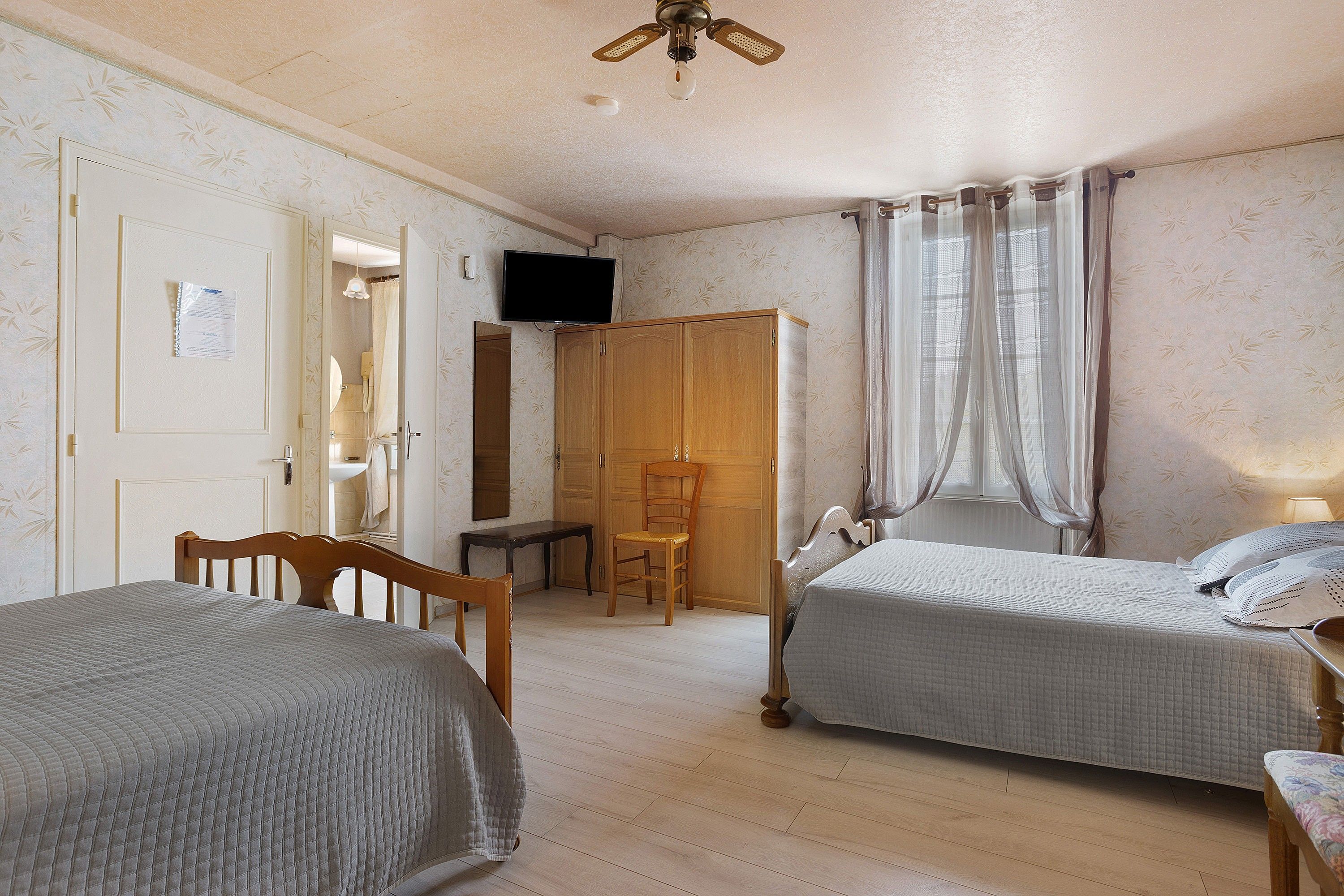 Quarto com duas camas, guarda-roupa de madeira, escrivaninha e televisão.