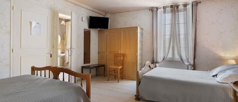 A bedroom with two beds, a wooden wardrobe, a desk, and a television.