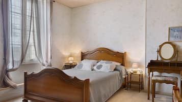 Quarto com cama de madeira, duas mesas de cabeceira com luminárias, uma cadeira e um espelho.