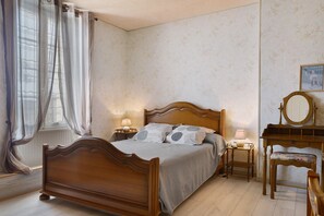 Ein Schlafzimmer mit einem hölzernen Bett, zwei Nachttischen mit Lampen, einem Sessel und einem Spiegel.