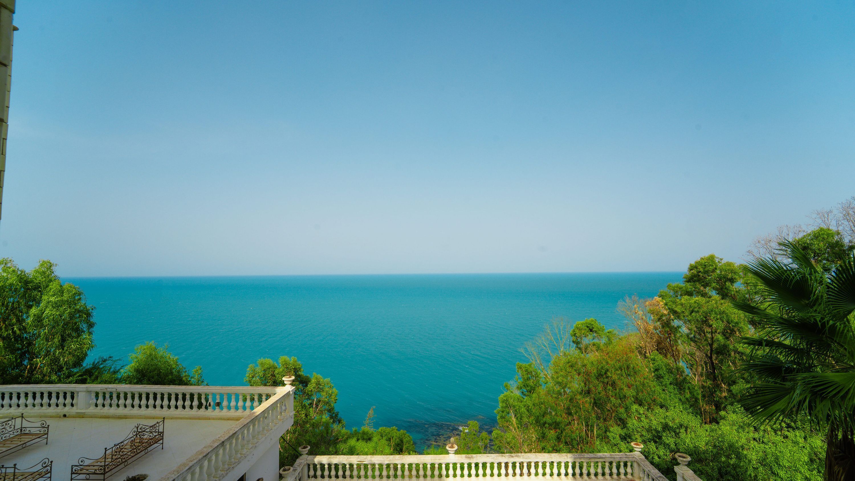 A balcony overlooking a clear blue sea with lush greenery in the foreground.