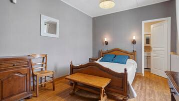 Ein Schlafzimmer mit einem hölzernen Bett, einem Nachttisch, einem Stuhl, einer Holzbank, einem Spiegel und einer Tür zu einem Badezimmer.