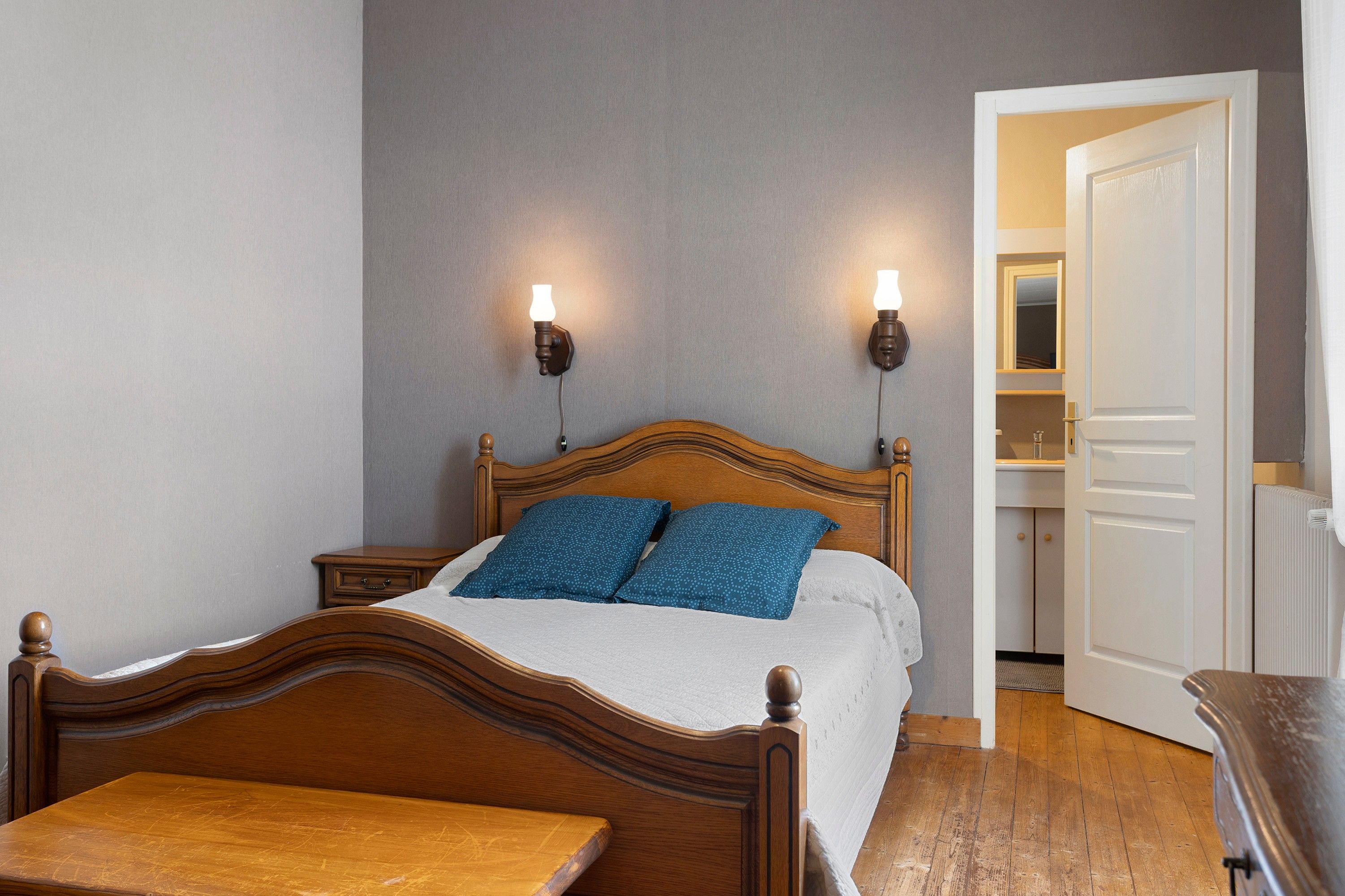 A bedroom with a wooden bed, two bedside tables, a nightstand, a wooden bench, and a door leading to a closet.