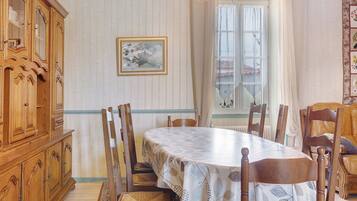 A dining room with a large wooden table, chairs, a cabinet, and a window with curtains.