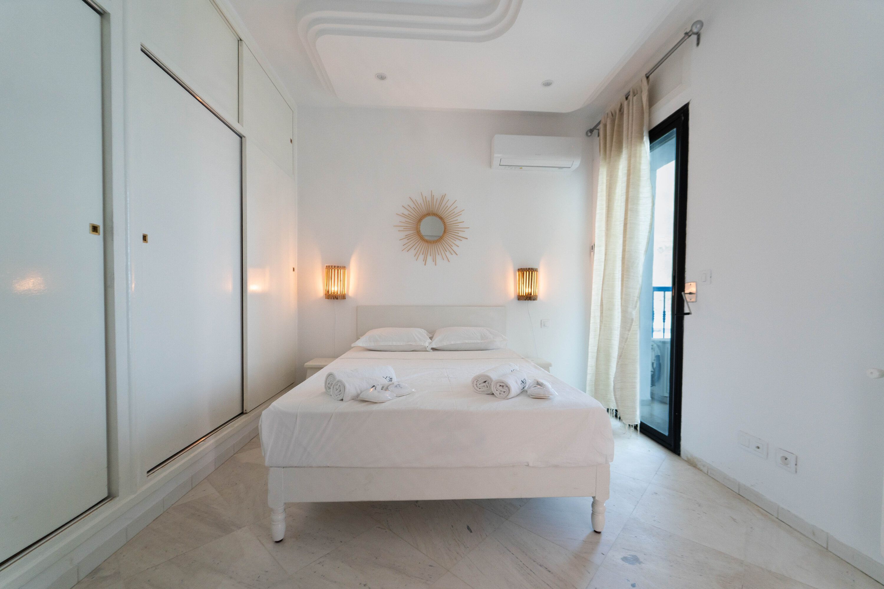 Una camera d'albergo con un letto grande, due lampade ai piedi del letto, una decorazione a forma di sole e una porta scorrevole in vetro.