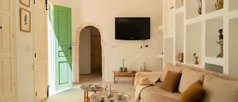 A living room with a beige sofa, a television mounted on the wall, and a green door leading to another room.