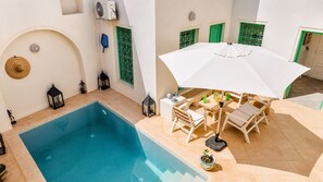 Een zwembadterras met een zwembad, tuinmeubels en een witte parasol.