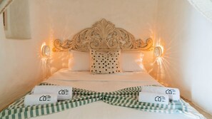 A hotel room with a decorative headboard, two wall-mounted lights, a bed with white bedding, and a checkered green and white striped blanket. - Dar Dada Djerba: Maison traditionnelle Houch (Djerba Midun)
