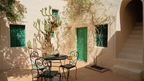 A courtyard with a table and chairs, a cactus, and a staircase. - Dar Dada Djerba: Maison traditionnelle Houch (Djerba Midun)