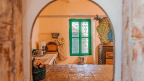 Un corridoio stretto con una finestra con cornice verde, una piccola zona cucina con frigorifero e un muro decorato.