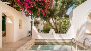 A pool area with a stone border, a bench, and a door leading to a covered space. - Dar Dada Djerba: Maison traditionnelle Houch (Djerba Midun)