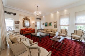 A spacious living room with a red patterned carpet, a chandelier, and multiple seating options including sofas and armchairs. - Villa d'exception à Gammarth – piscine privée (Gammarth)