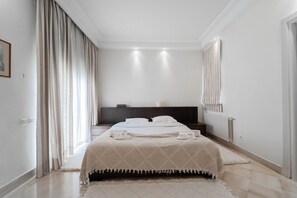 Une chambre d’hôtel avec un lit, une table de chevet, une commode, un radiateur et une fenêtre avec des rideaux.